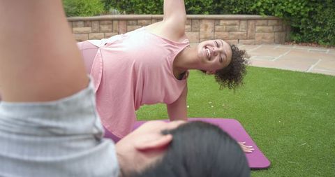 Friends practicing side-plank on backyard lawn smiling during outdoor fitness session
