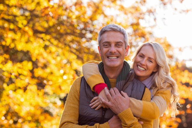 Middle-aged couple enjoying a sunny autumn day in the park, surrounded by golden leaves. Perfect for themes of love, happiness, nature, and seasonal activities. Ideal for use in advertisements, greeting cards, and lifestyle blogs.