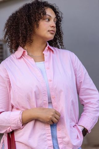 Mid-20s african american woman standing and glancing right wearing pastel pink shirt with red tote