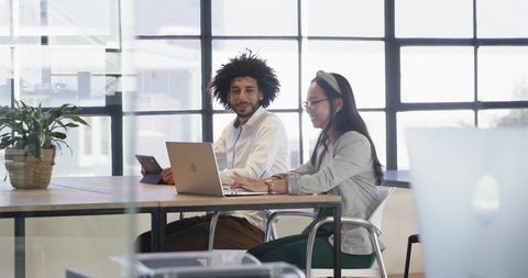 Multicultural coworkers collaborating on laptop and tablet in modern open-plan daylight office