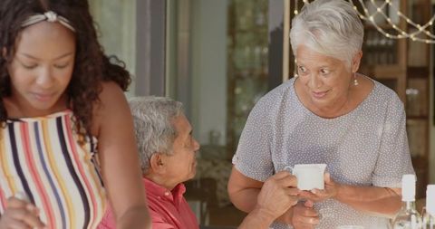 Multigenerational family serving coffee and preparing meal at sunlit dining table at home