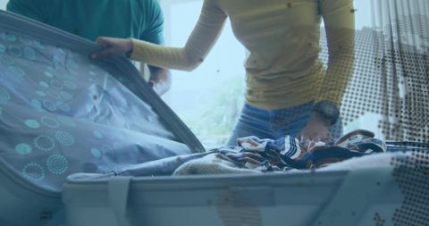 Couple packing hardshell suitcase together preparing casual weekend trip by sunlit window