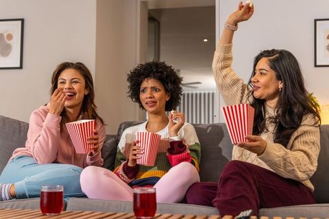 Friends enjoying movie night on couch sharing popcorn and laughing in cozy knitwear