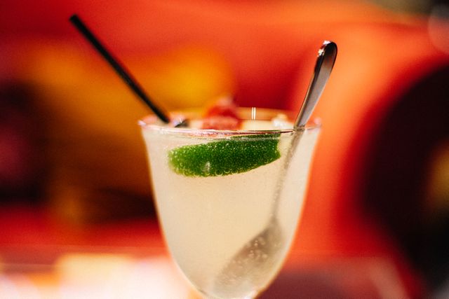 Close-up of refreshing lime cocktail with a black straw and a spoon. Ideal for use in bar or restaurant advertisements, cocktail recipes, summer party invitations, or lifestyle blogs.