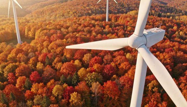 Spinning wind turbine overlooking autumn forest with golden foliage, renewable energy
