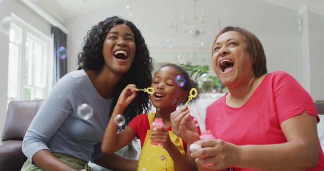 Three generations of women are enjoying quality time together at home. Blowing bubbles, the scene captures priceless expressions of joy and laughter, making it an ideal choice for advertisements or articles about family bonding, multigenerational living, or home life. This image evokes feelings of warmth, togetherness, and fun, suitable for websites, brochures, and promotions focused on family values and recreational activities.