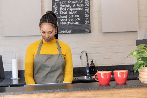 African american barista using pos tablet serving coffee with red cups at rustic cafe counter