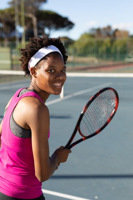 Smiling african american young female tennis player looking over shoulder while playing at court. unaltered, sport, competition and tennis game concept.