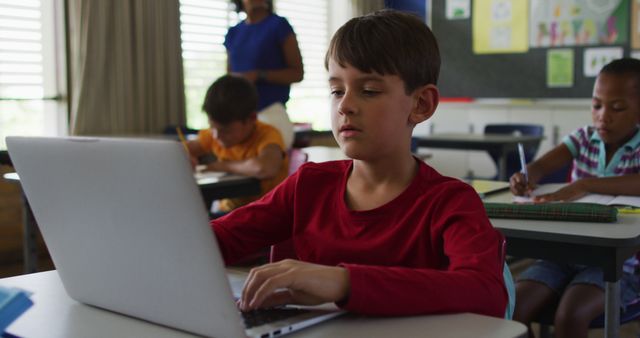 Portrait of happy caucasian schoolboy sitting at classroom, using laptop, looking at camera. children at primary school in summer.