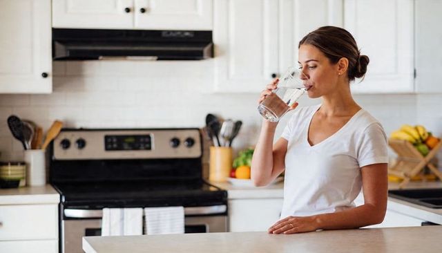 Woman drinking water at kitchen counter in bright modern minimalist home interior