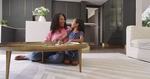 Diverse mother and daughter drawing with crayons on floor in modern living room