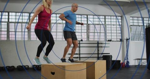 Partners performing synchronized box jumps on plyo boxes in bright indoor fitness studio