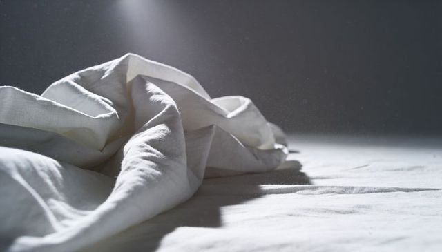 Crumpled white linen sheets sculpting soft folds under dramatic side light