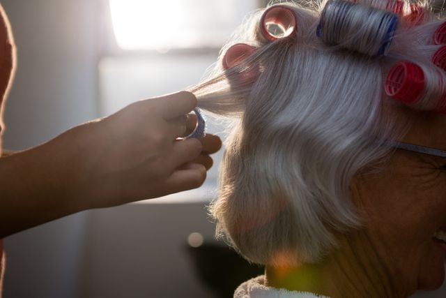 Cropped hands of hairstylist removing curlers from senior woman hair