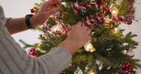 Mature man decorating Christmas tree with tinsel and baubles