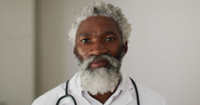 Portrait of african american senior male doctor with white hair and beard smiling to camera. staying at home in isolation during quarantine lockdown.