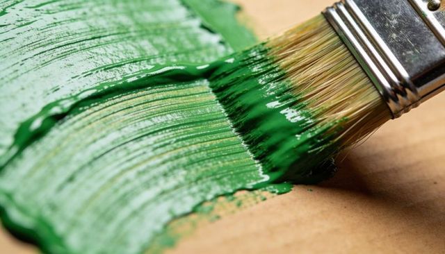 Spreading glossy green paint with flat-bristle brush on kraft paper macro texture