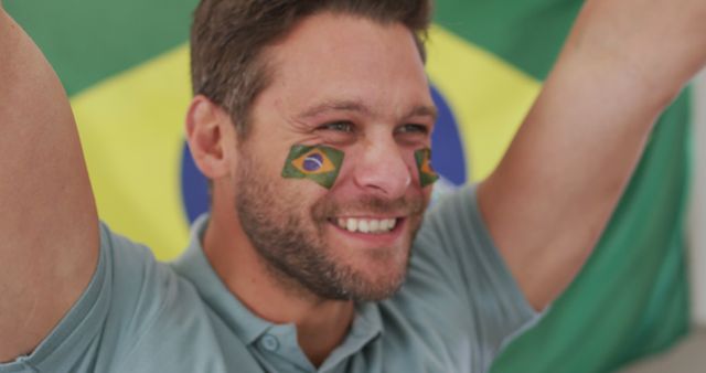 An enthusiastic man with Brazilian flag face paint smiling and celebrating. This is ideal for content related to sports events, Brazilian national celebrations, and fan reactions.