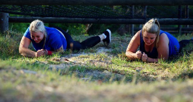 Two women crawling under a net during a team-building activity. They are dressed in sportswear and are smiling, suggesting camaraderie and enjoyment. Perfect for use in content promoting team-building exercises, fitness challenges, motivational events, and outdoor activities.