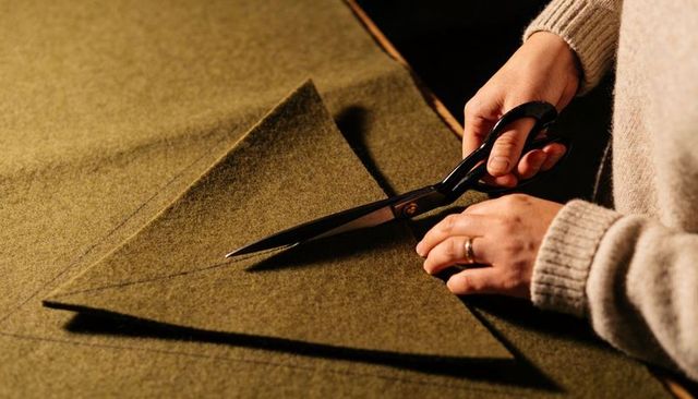 Cutting olive wool with tailor shears for precise garment tailoring