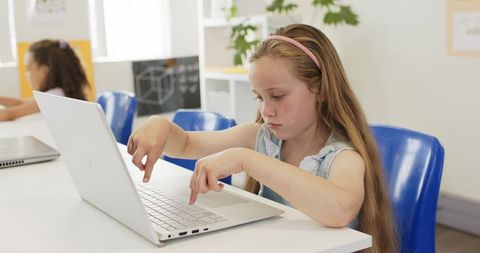 Young girl typing on laptop focusing on digital learning in bright classroom
