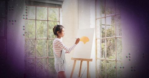 Young artist painting vibrant yellow brushstroke on canvas in calm sunlit studio