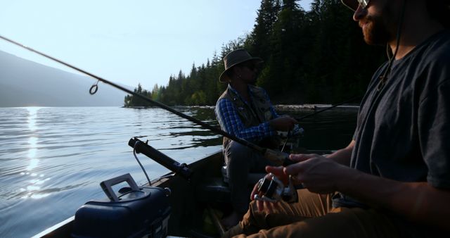 Two men cast fishing lines into a tranquil lake surrounded by lush forest. The setting sun adds warmth to the serene atmosphere. Ideal for promoting outdoor activities, leisure travel, nature experiences, and companionship.