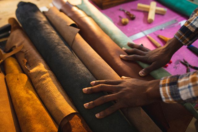 Cropped hands choosing from leather rolls on workbench in workshop. unaltered, small business, craftsmanship, handcraft, leather craft and workshop.