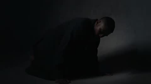 Kneeling man in low-key studio lighting reacting to narrow spotlight and dramatic shadows