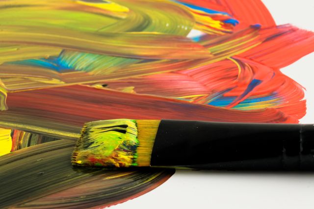 This close-up captures a paintbrush creating bold, colorful strokes on a canvas. Ideal for art-related content such as blogs about painting techniques, online art courses, and creative inspiration websites.
