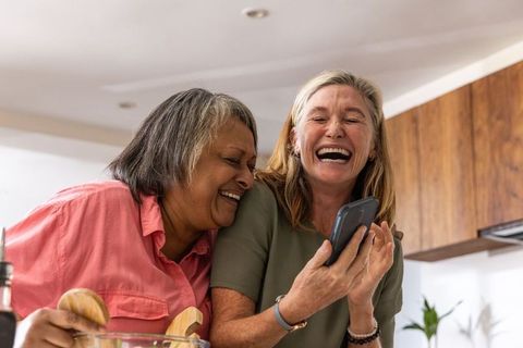 Senior Friends Laughing Together While Cooking in Kitchen
