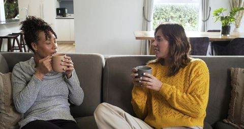 Friends chatting over coffee on cozy gray sectional sofa in bright open-plan living room