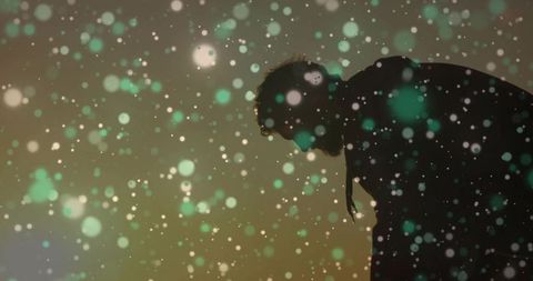 Moody silhouetted man bowing head with bokeh particles, backlight haze and stage light orbs
