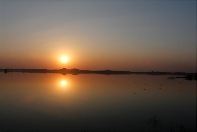 This captivating sunset with the sun setting over a calm lake reflects the natural beauty and tranquility of the location. Perfect for use in promotions related to travel, nature retreats, and landscape photography.