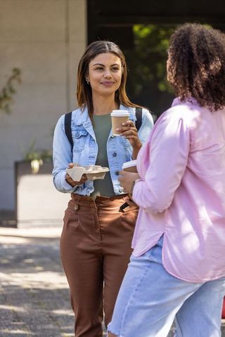 African women chatting with takeaway coffee in urban courtyard, casual friendship moment