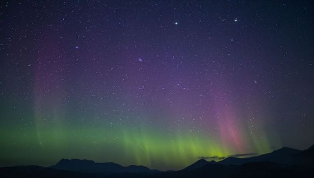 Aurora borealis glowing over mountain silhouette with green and purple bands and star-filled sky