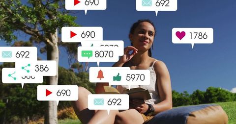 Woman reading book in park surrounded by social media notifications