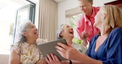 Elderly Friends Laughing Together with Tablet in Living Room