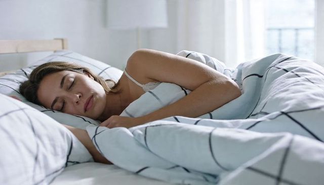 Woman sleeping peacefully in minimalist sunlit bedroom with grid duvet and lace camisole