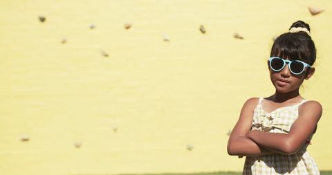 Confident young girl in sunglasses against vibrant yellow wall