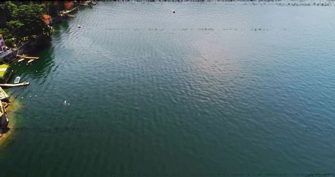 Sunlit lake rippling with swimmers, docks and buoys from high aerial perspective