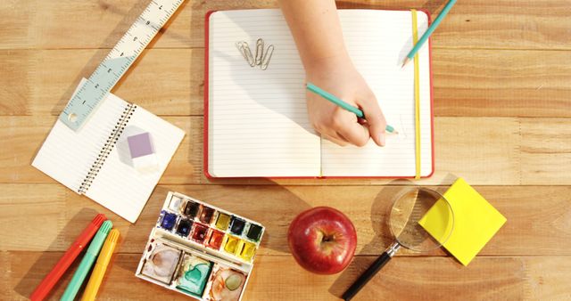 Perfect illustration of a student's desk with essential study supplies including notebooks, pens, watercolor palette, apple, and organization tools. Ideal for educational content, school materials, back-to-school promotions, and creative workshops. Highlights a clean, organized workspace conducive to learning and creativity.