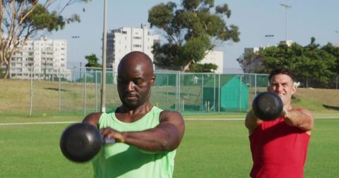 Men in outdoor exercise swinging kettlebells on sports field