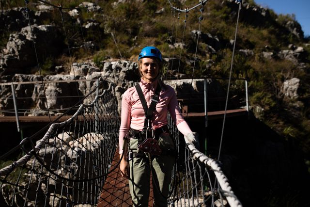 Caucasian woman enjoying an outdoor adventure, wearing zip lining equipment and smiling at the camera. Ideal for promoting outdoor activities, adventure tourism, travel destinations, and safety gear. Perfect for use in travel blogs, adventure sports advertisements, and vacation planning materials.