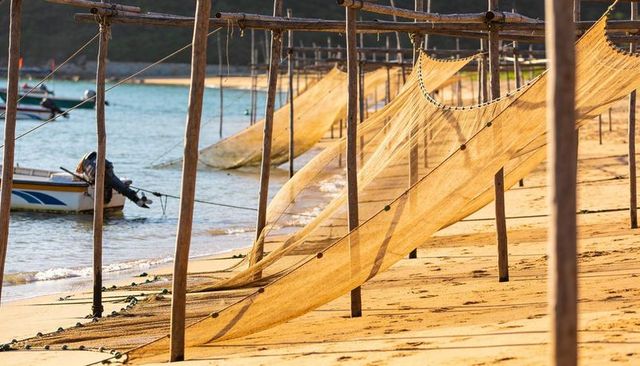 Golden fishing nets drying on tropical sandy shoreline with wooden poles and mooring boat