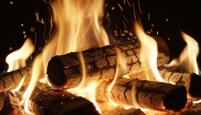 Crackling charred logs burning in fireplace with glowing embers and flying sparks