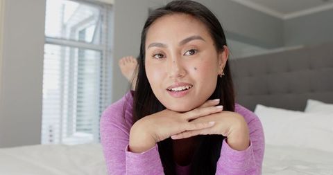 Asian Woman Relaxing on Bed in Cozy Bedroom Setting