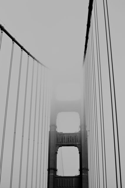 Vertical shot of iconic Golden Gate Bridge enveloped in thick fog, creating a dramatic atmosphere. Ideal for travel-related content, brochures, and architectural studies, emphasizing the mystique and monumental nature of this famous landmark.