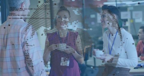 Colleagues chatting over coffee by glass partition in modern open office workspace