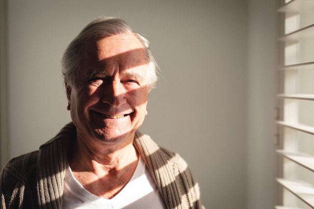 Portrait of caucasian senior man smiling near the window at home. retirement senior lifestyle living concept